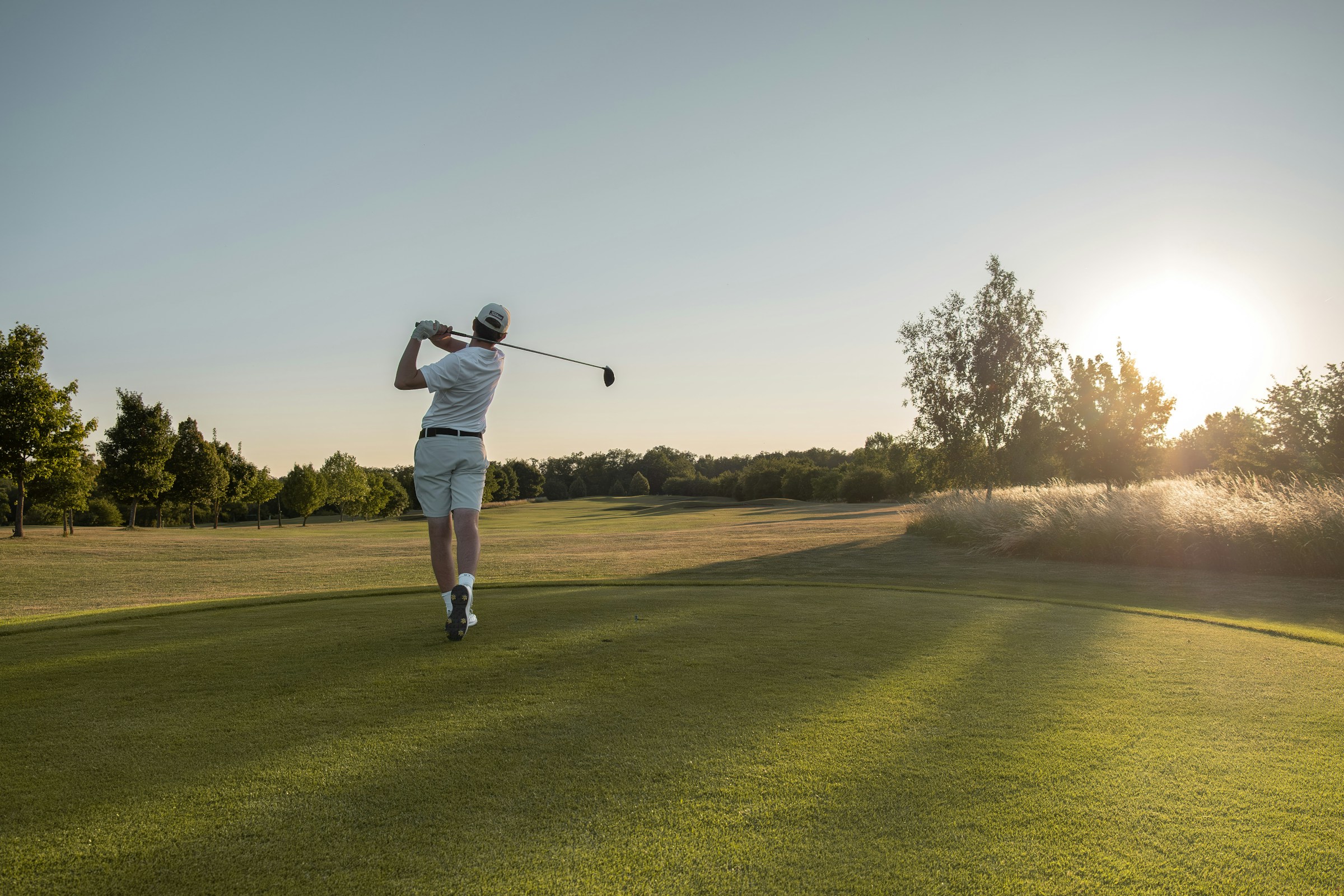 Golfer completing a drive at sunset