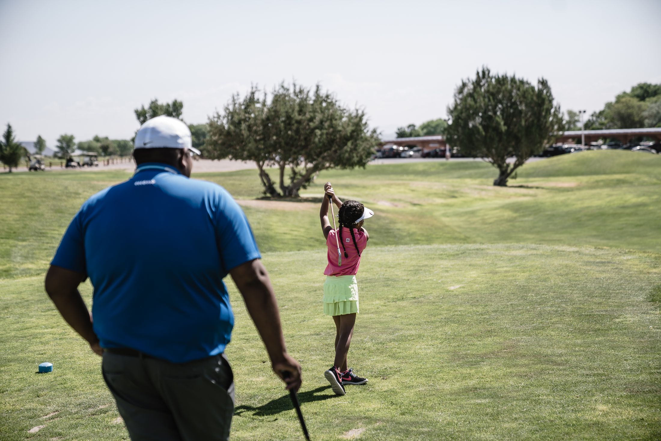 Junior golfer completing a drive with a coach nearby